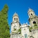 2 cypress trees standing next to the ornate bell towers of a Gothic church